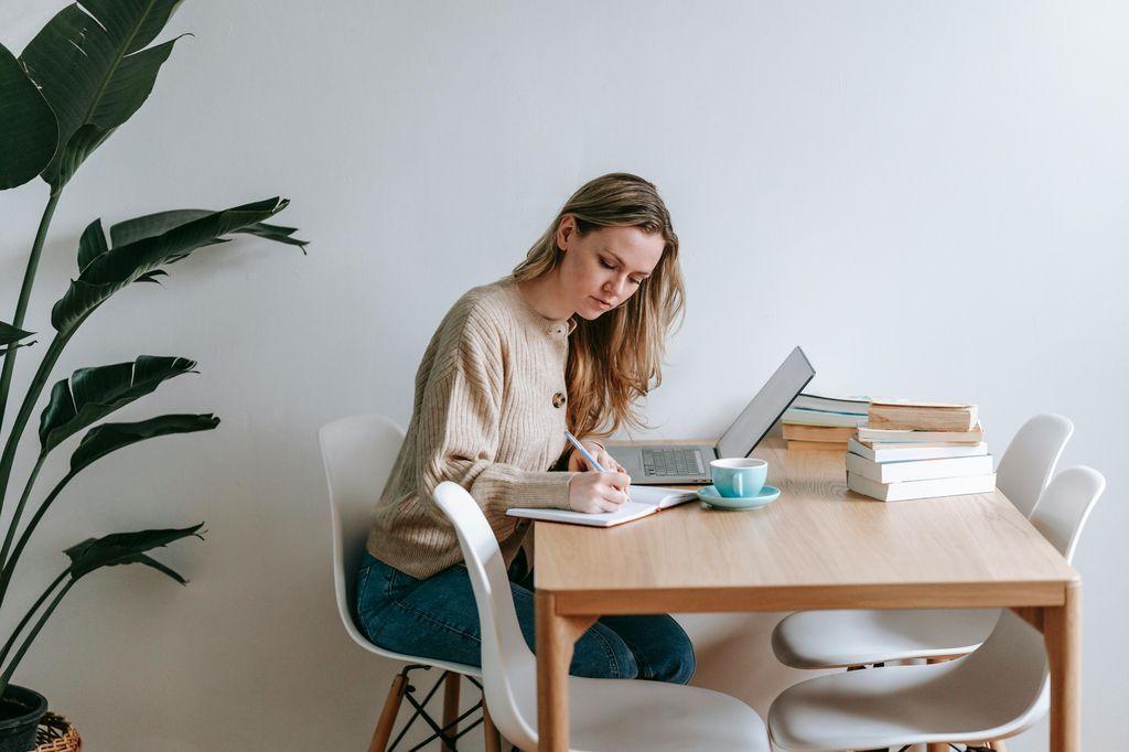 uma mulher sentada à mesa com um laptop e uma planta