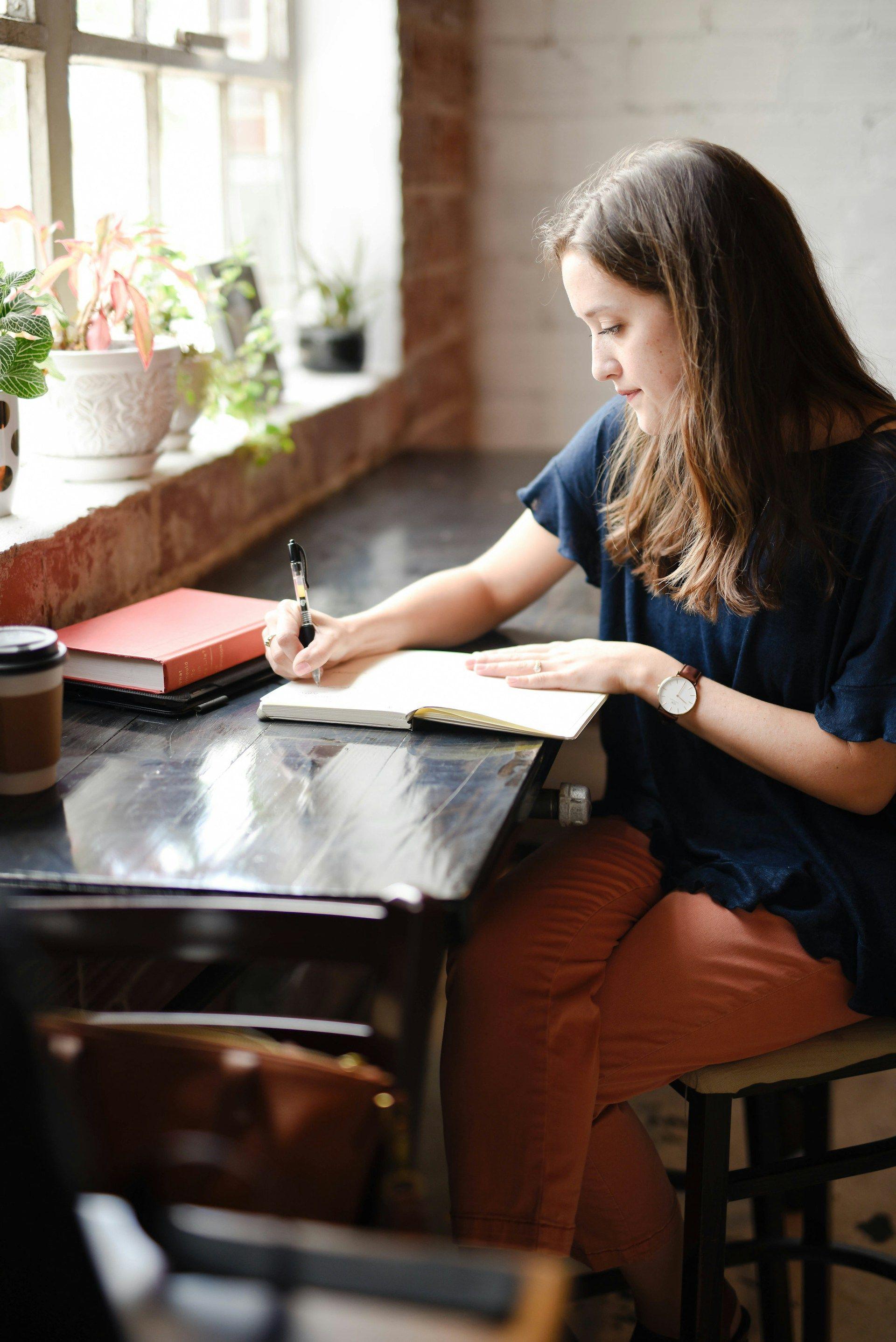 uma mulher sentada em uma mesa escrevendo em um caderno