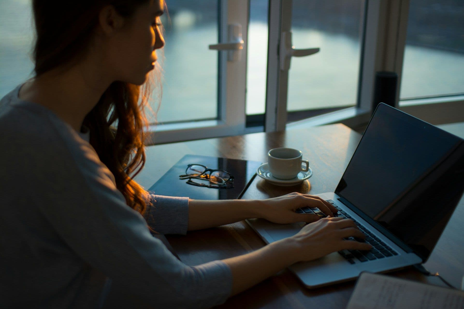 uma mulher trabalhando em um laptop em frente a uma janela