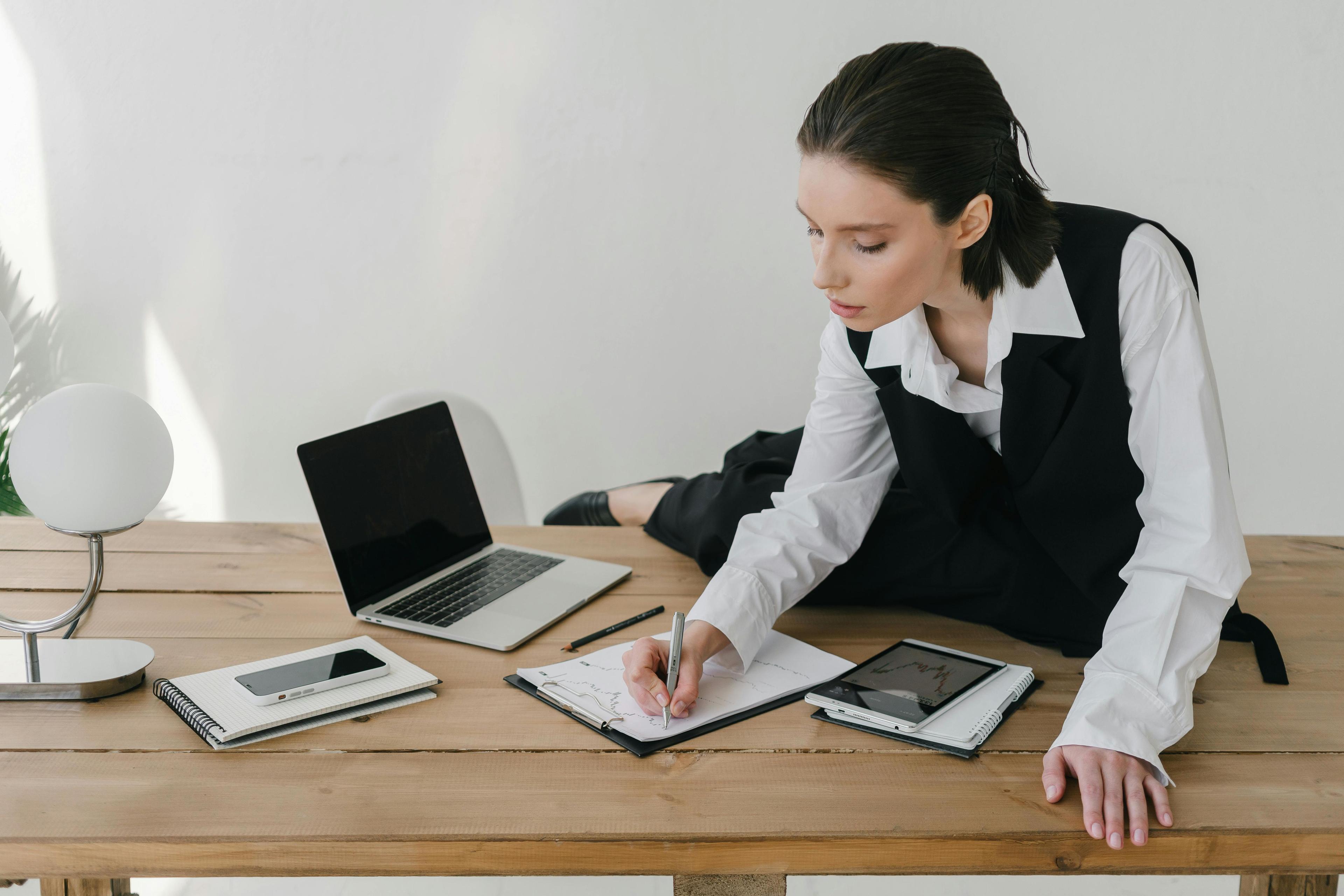 a business woman sitting at a desk with a laptop and a notebook