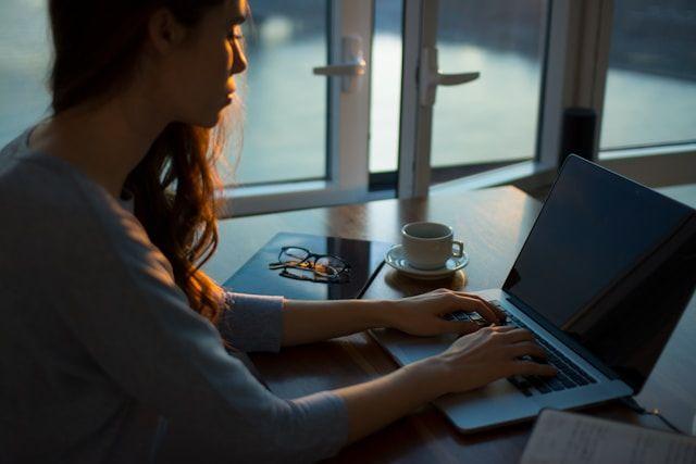 een vrouw die werkt op haar laptop voor een raam