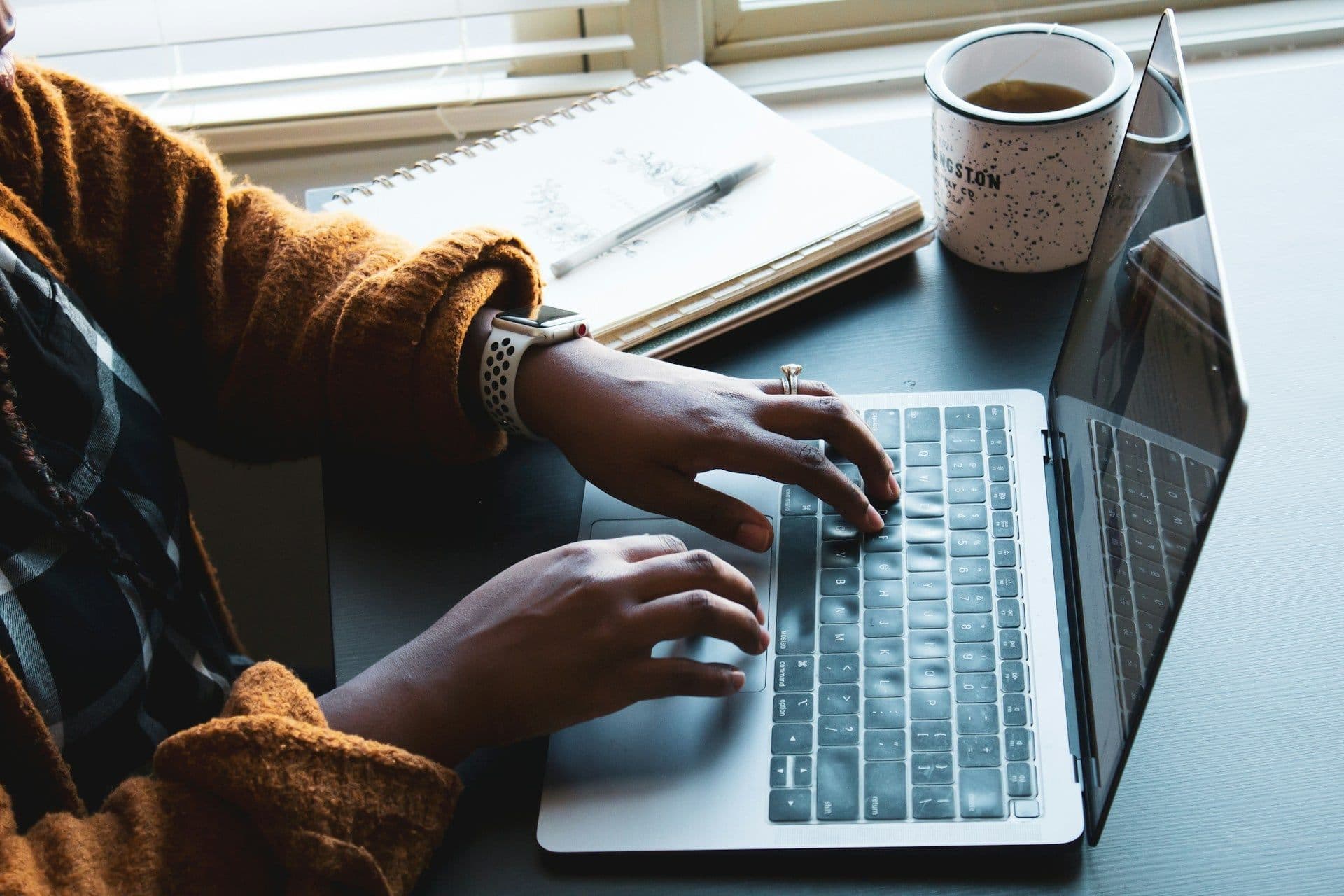 uma mulher digitando em um laptop com uma xícara de café