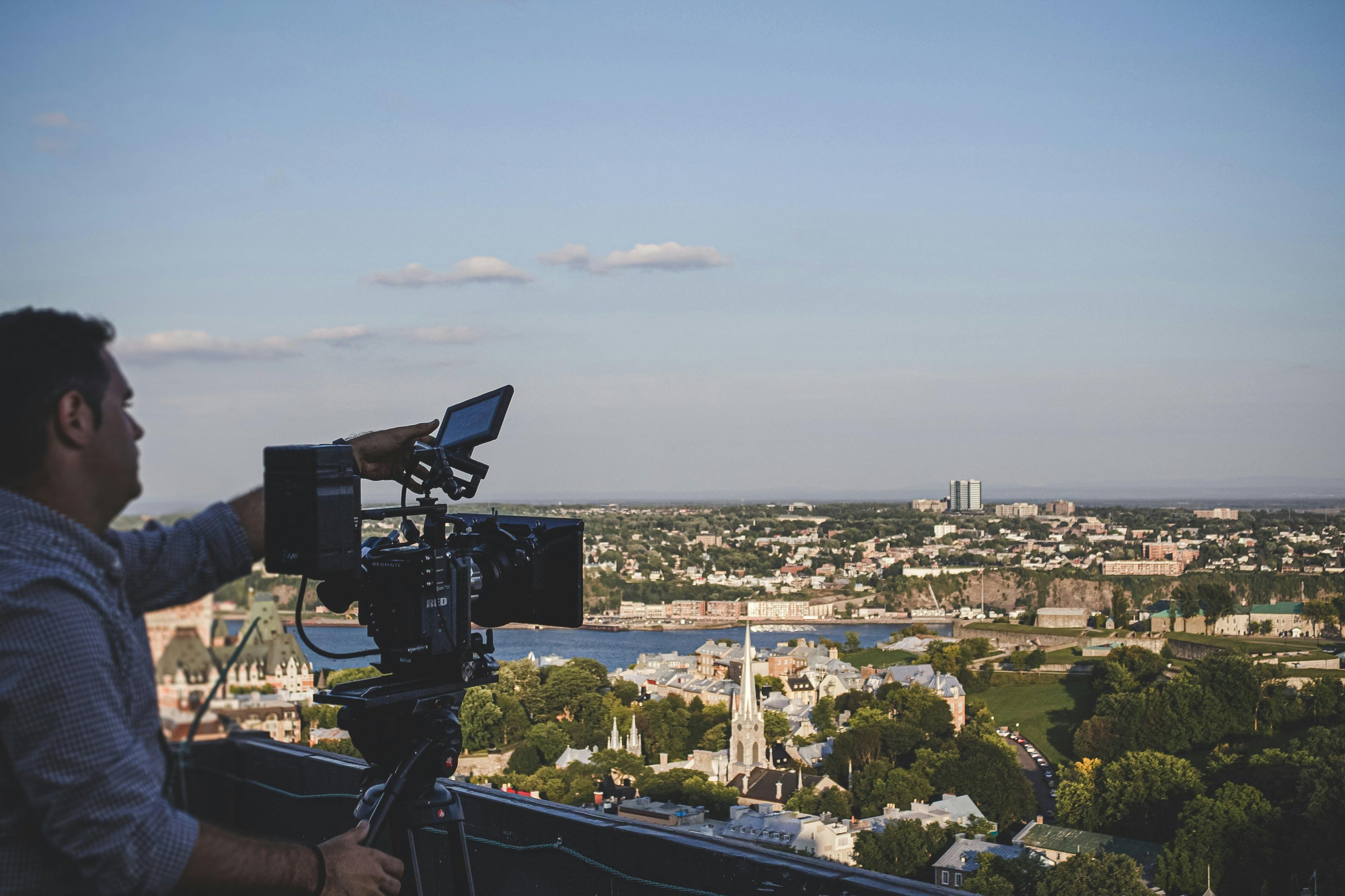 a man holding a camera on a rooftop overlooking a city