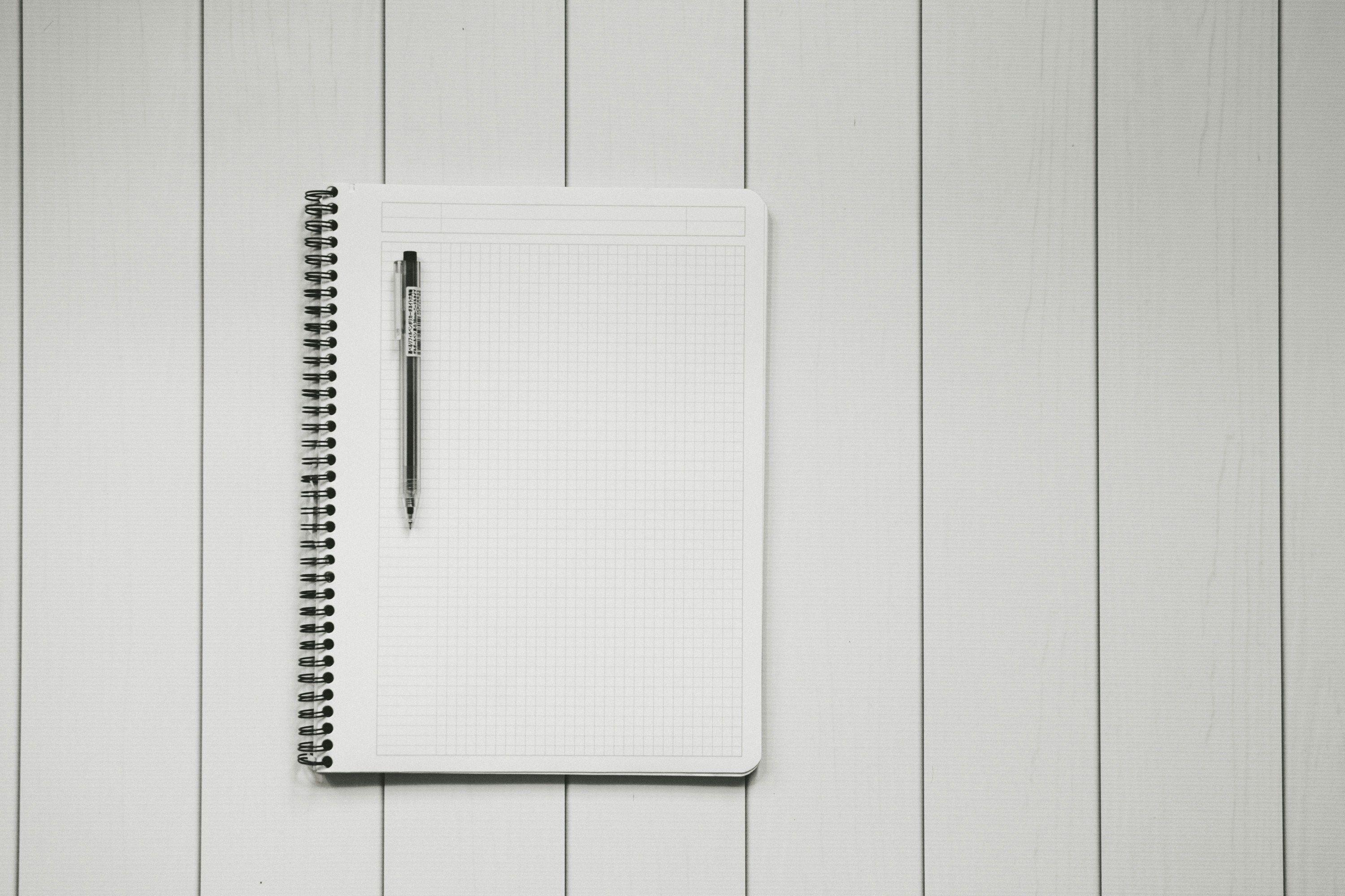 um caderno branco com uma caneta em um fundo de madeira