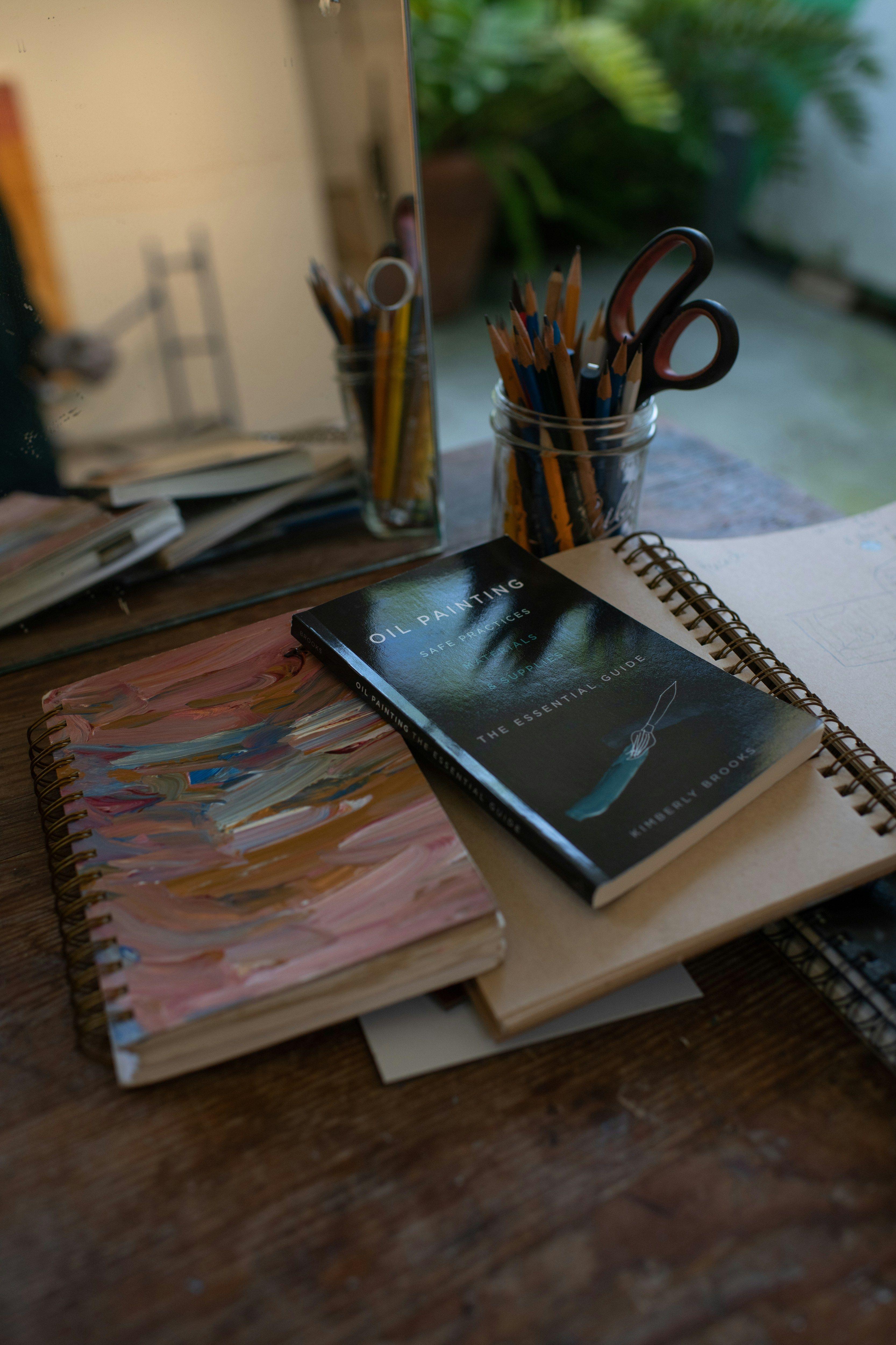 a desk with a notebook, pencils, and a mirror