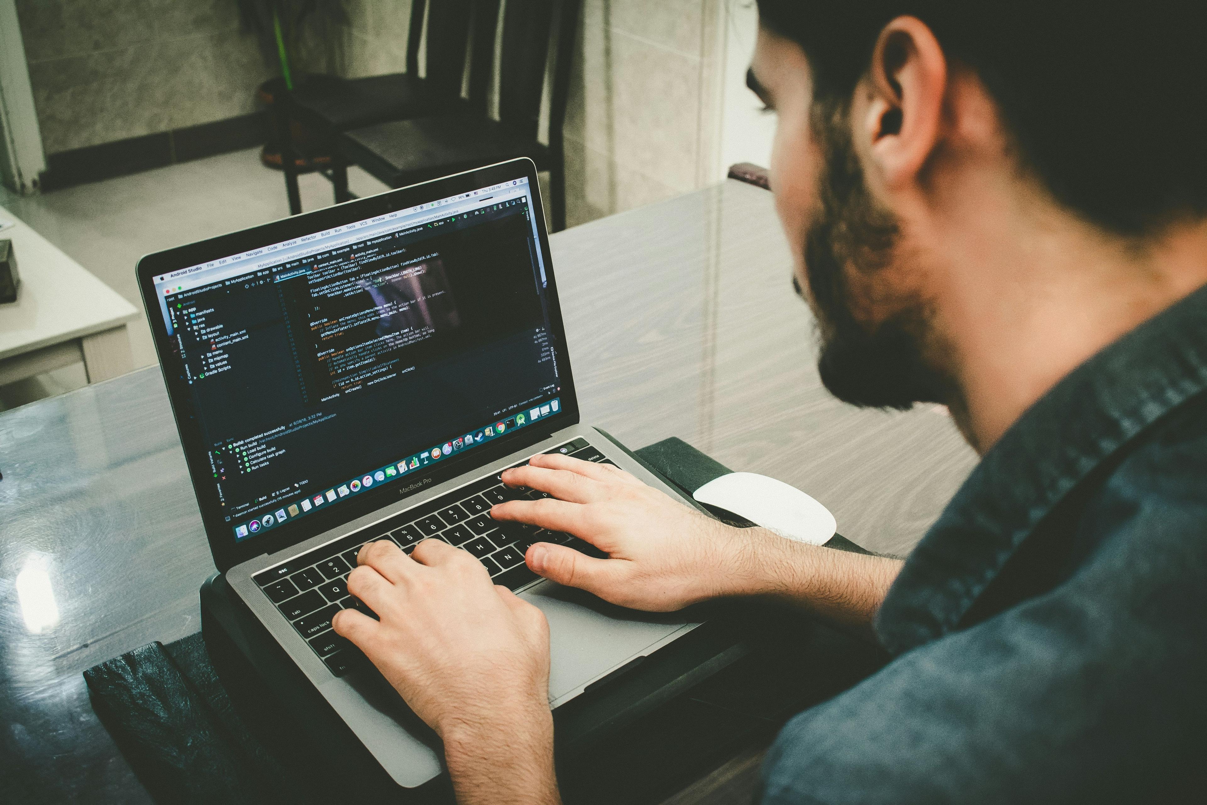 un hombre trabajando en una laptop con código en la pantalla