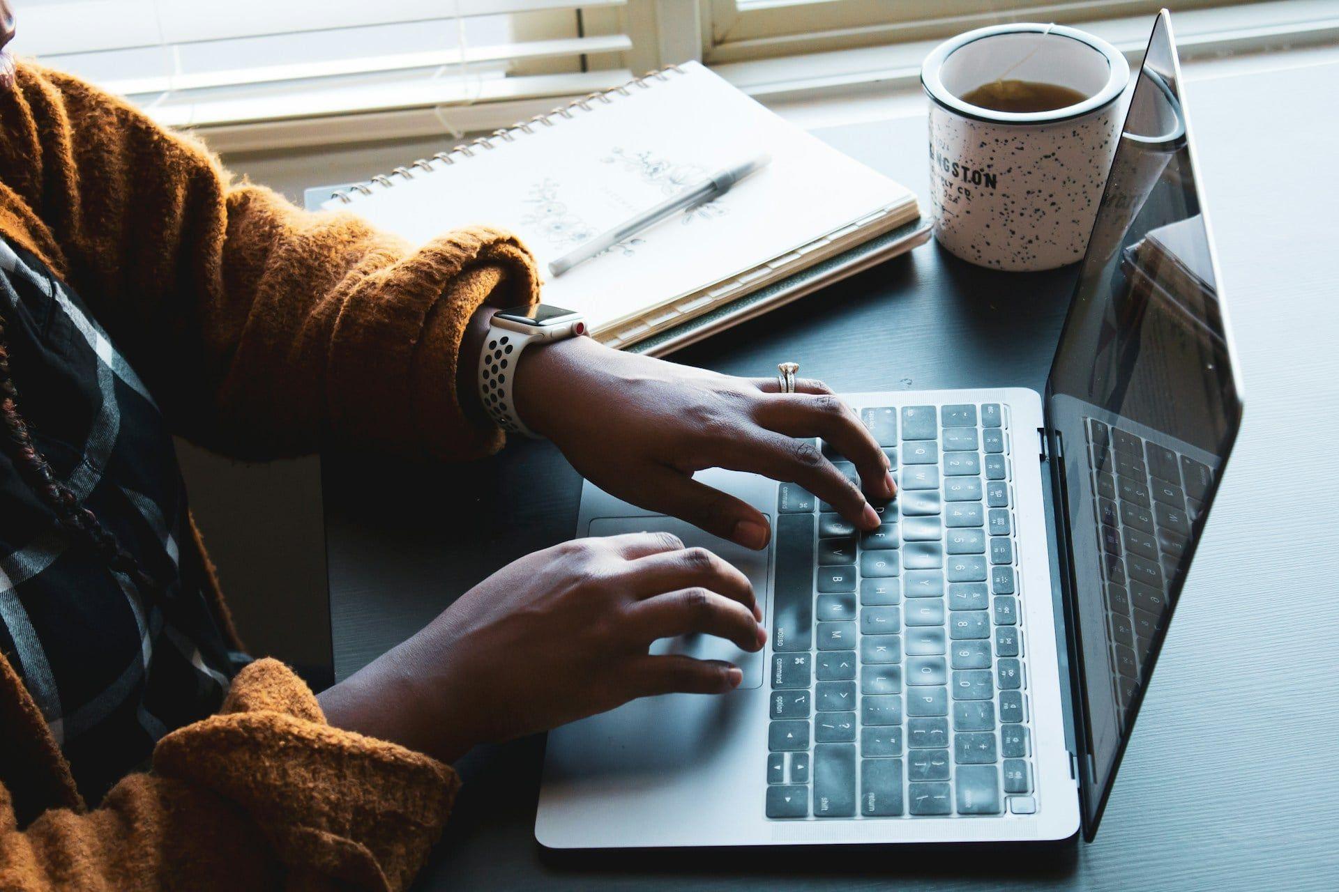 una mujer escribiendo en una laptop con una taza de café