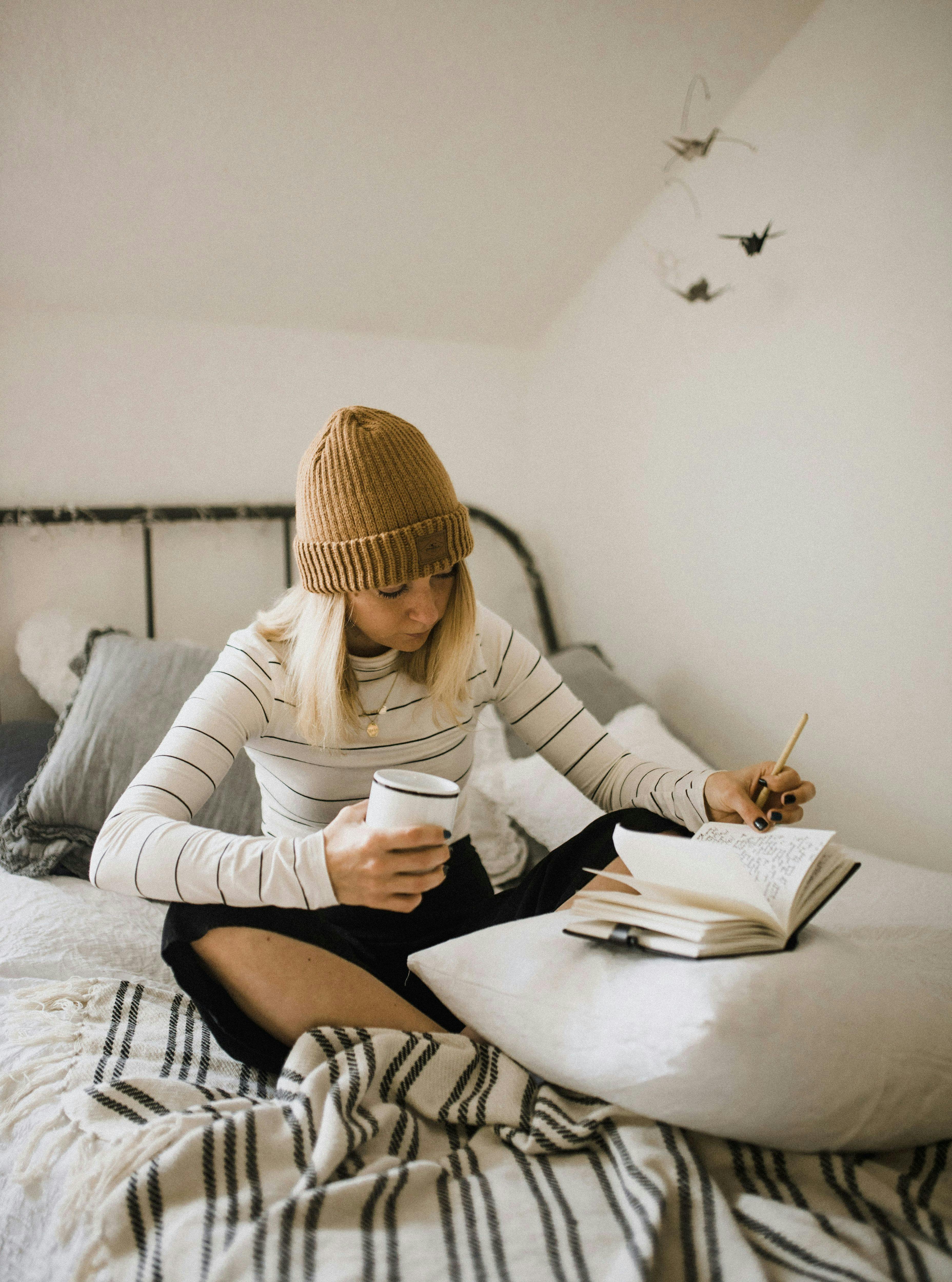 une femme assise sur un lit avec un livre et une tasse de café