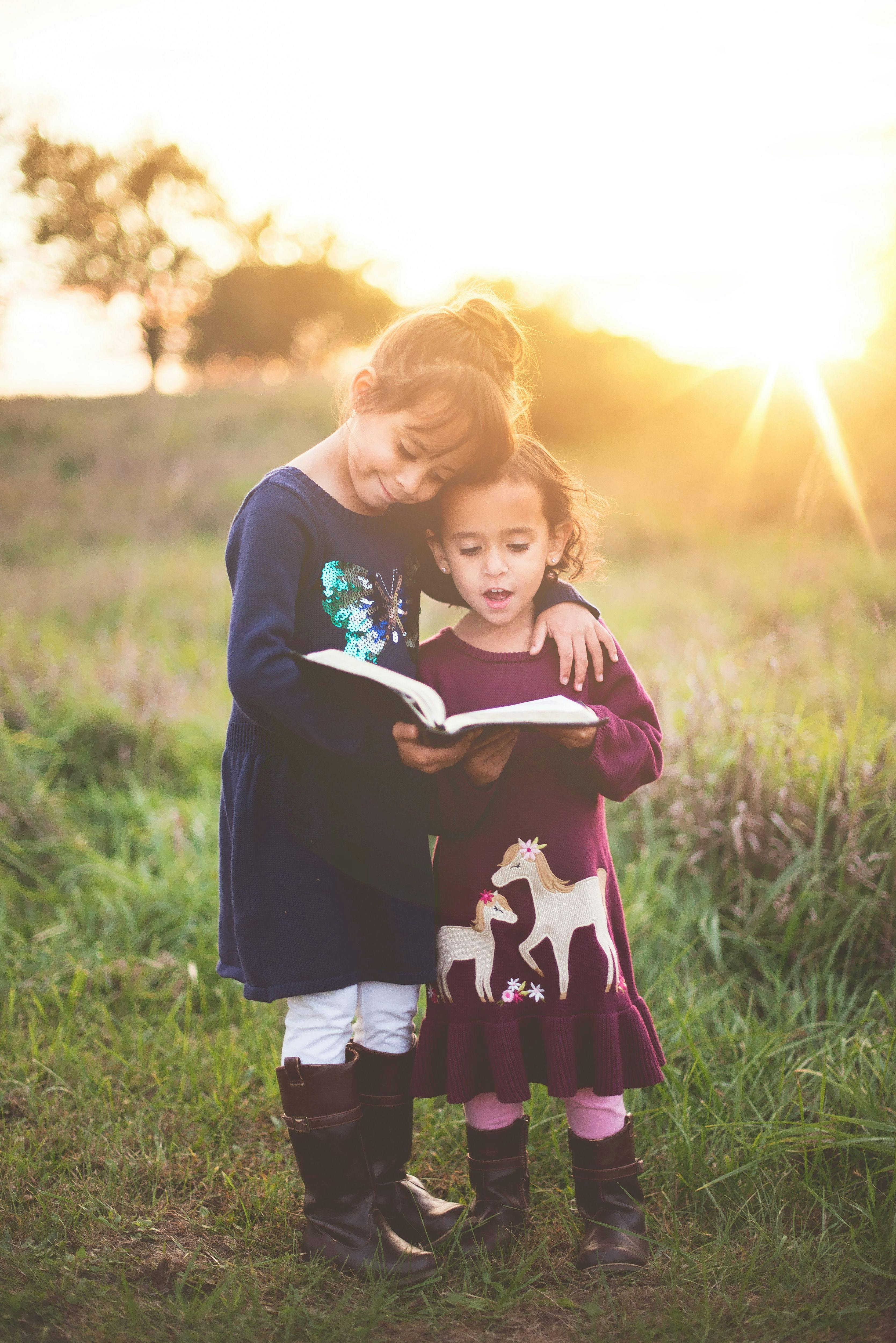 deux petites filles lisant un livre dans un champ au coucher du soleil