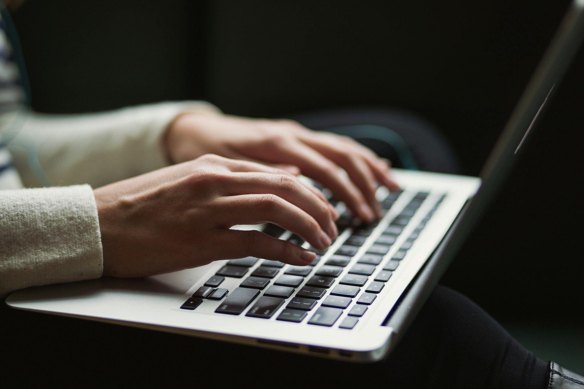 a woman's hands typing on a laptop