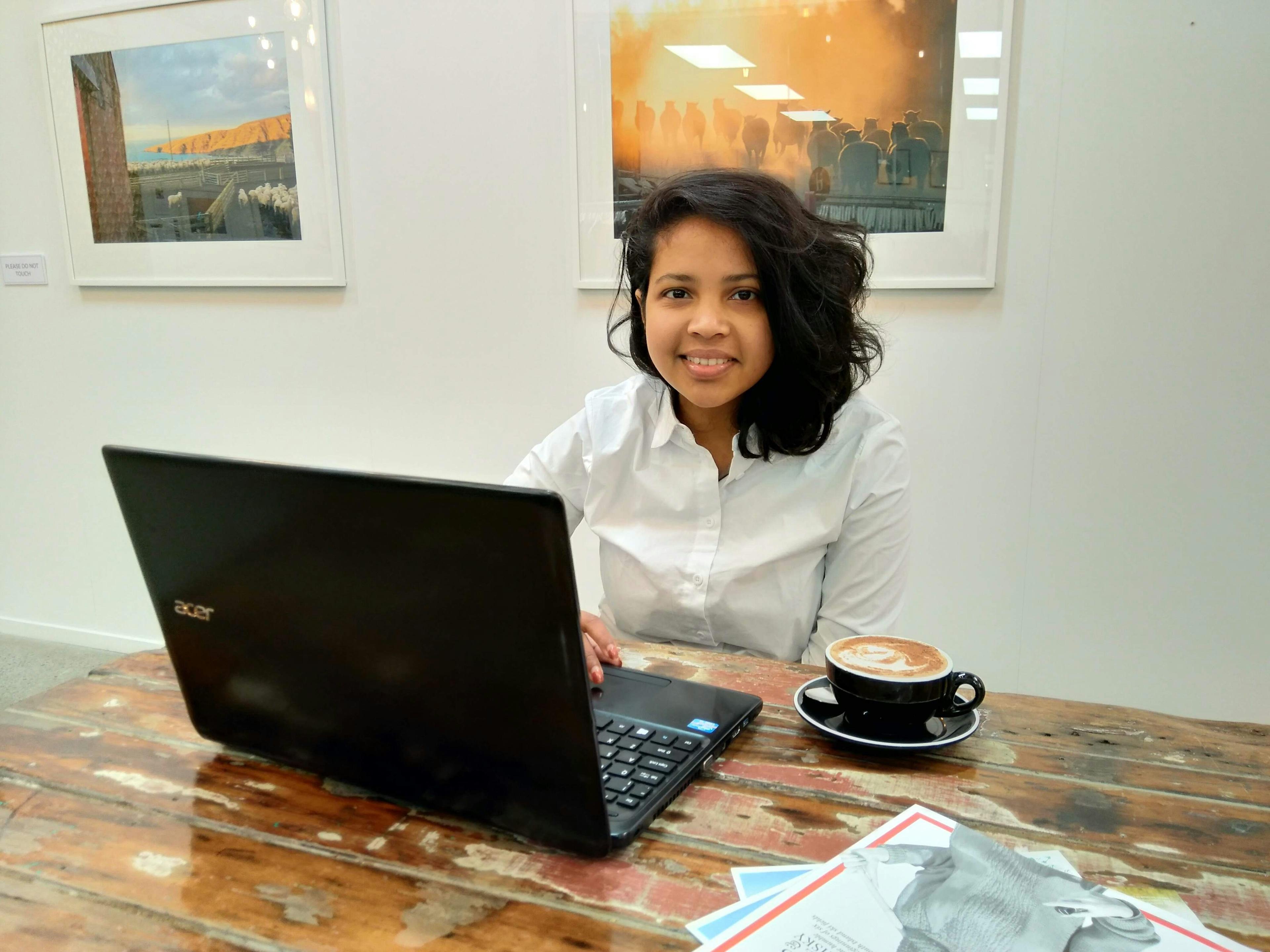 een vrouw zittend aan een tafel met een laptop en een kop koffie