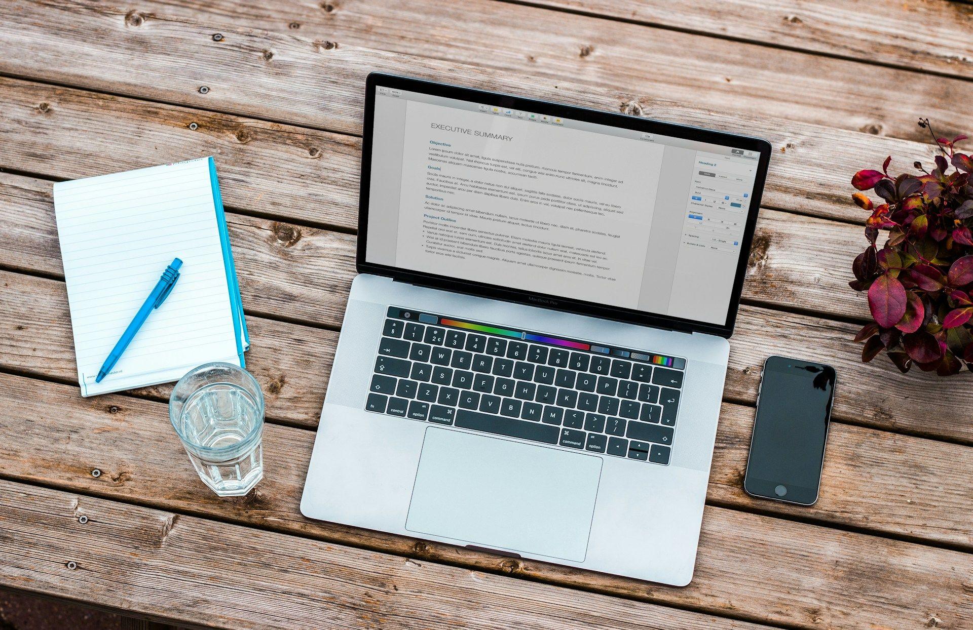 a laptop on a wooden table with a notebook and a phone