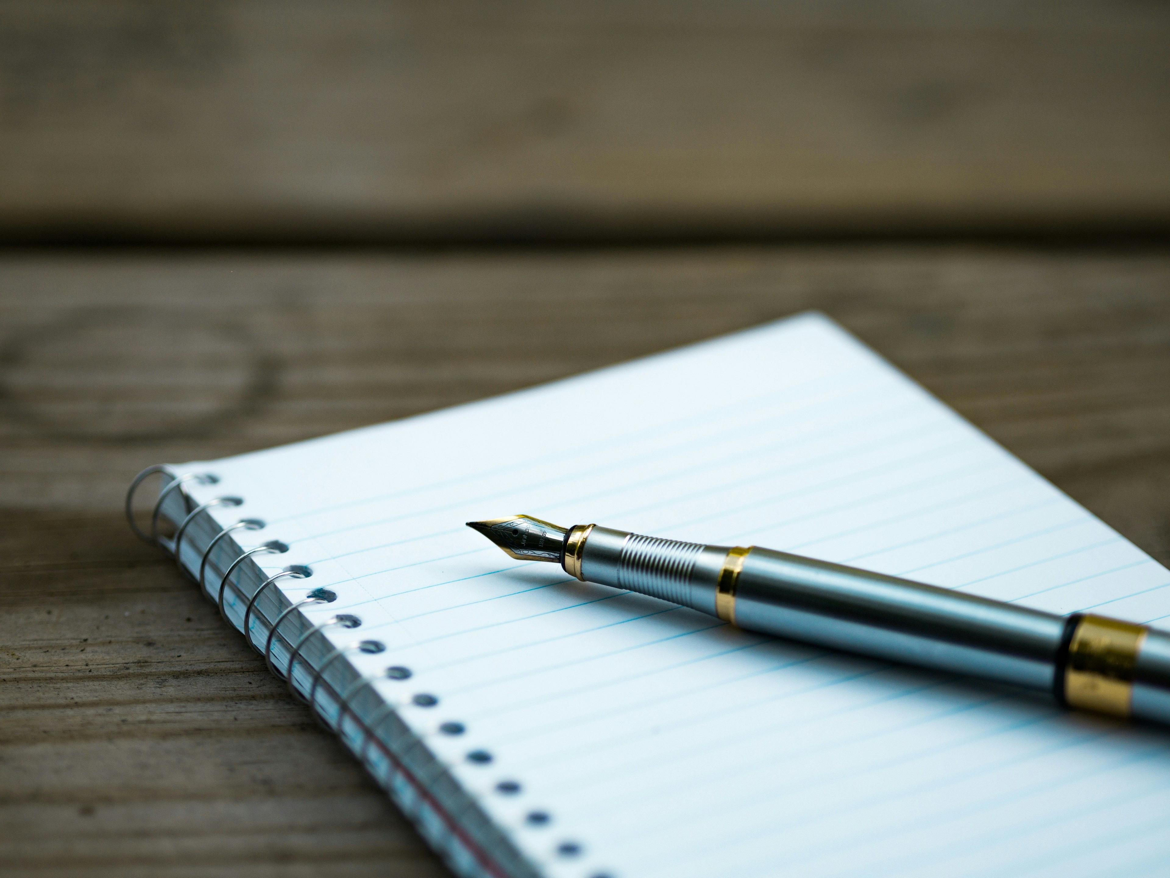 a pen on top of a notebook on a wooden table