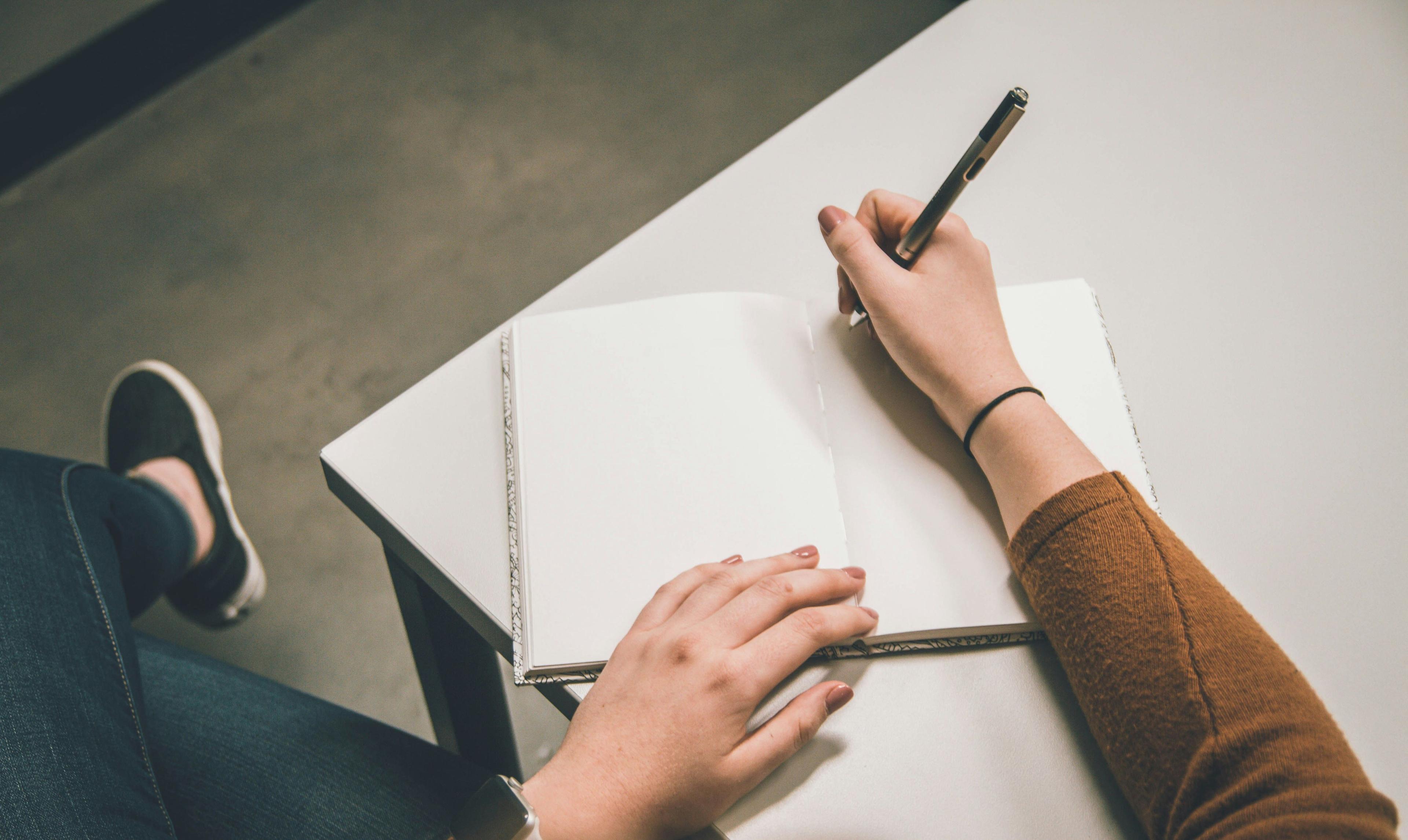 a woman writing in a notebook with a pen