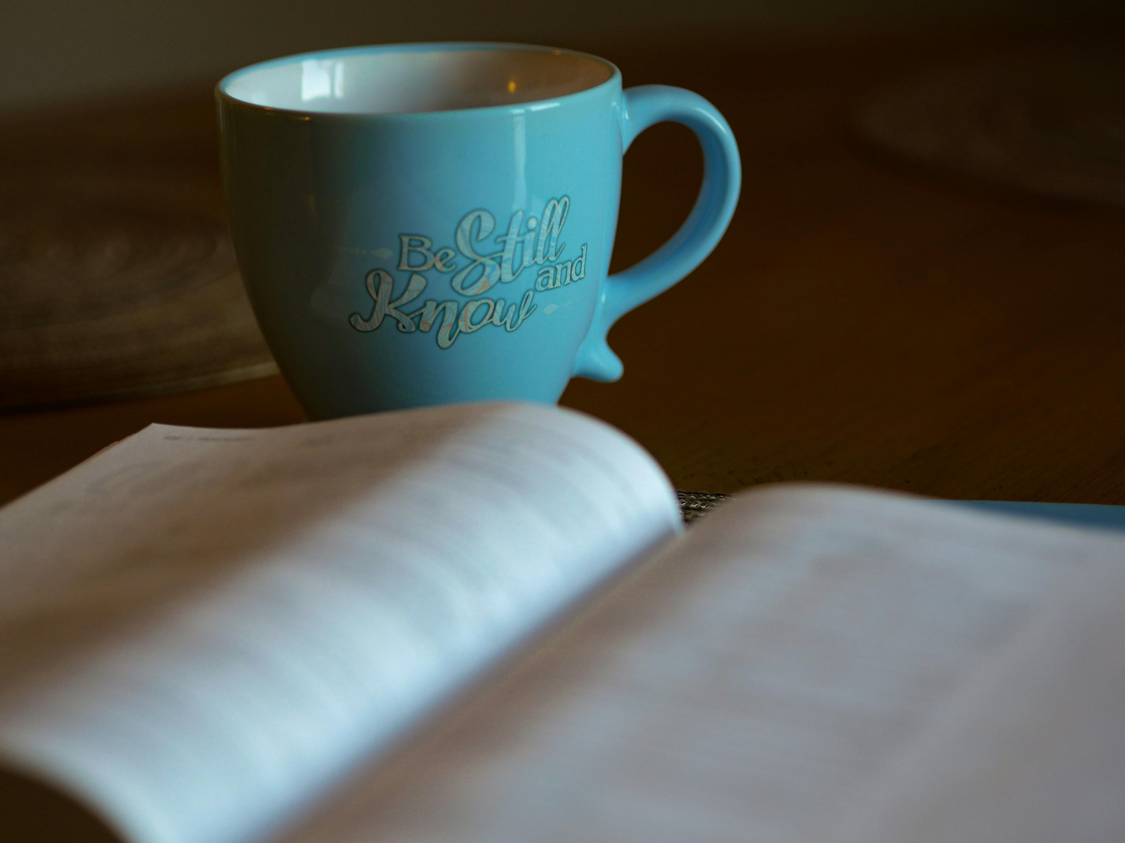 a blue coffee mug sitting next to an open book