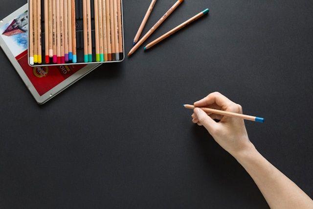 a woman's hand holding colored pencils on a black background