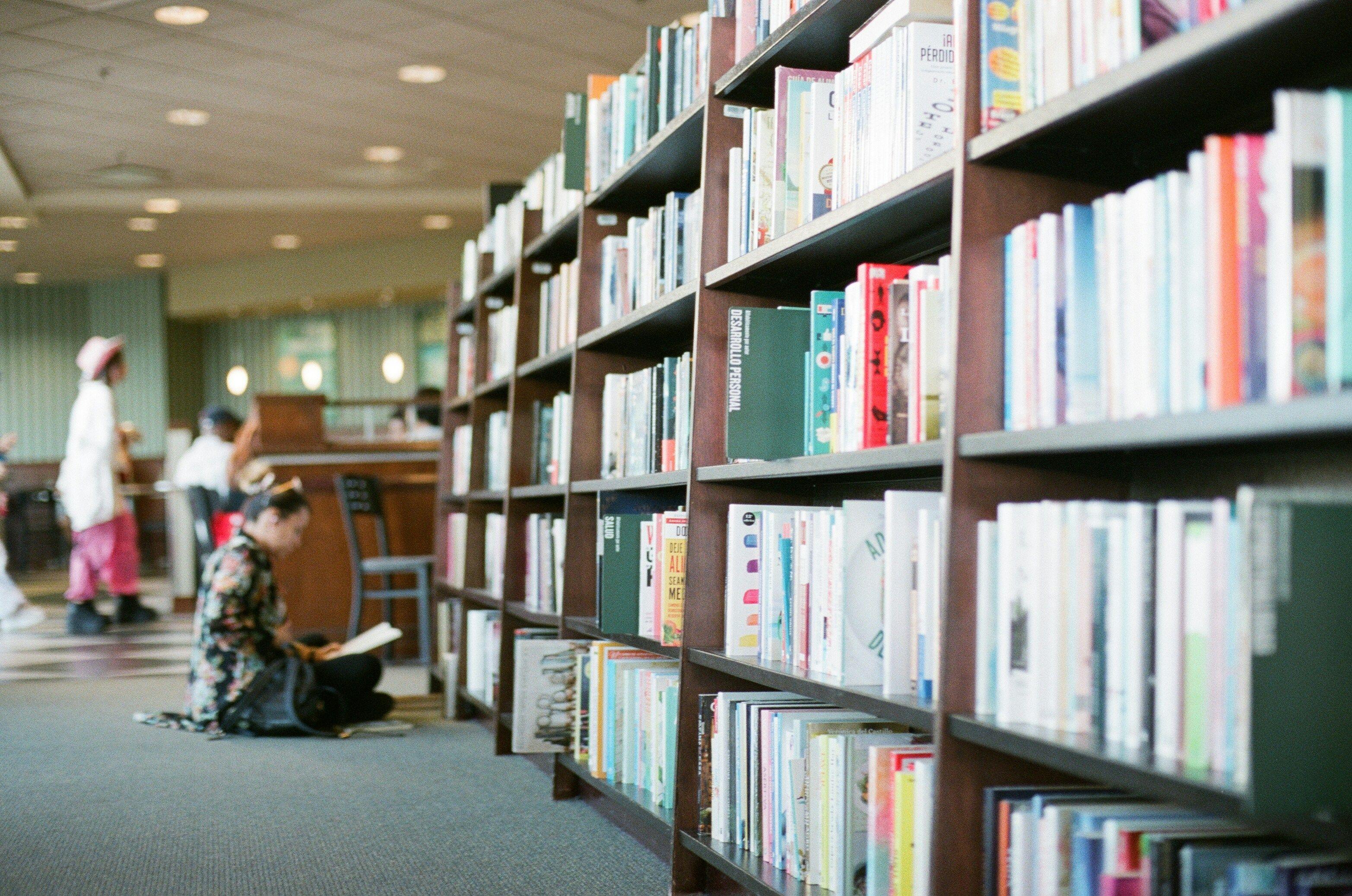 una persona seduta sul pavimento davanti a una libreria