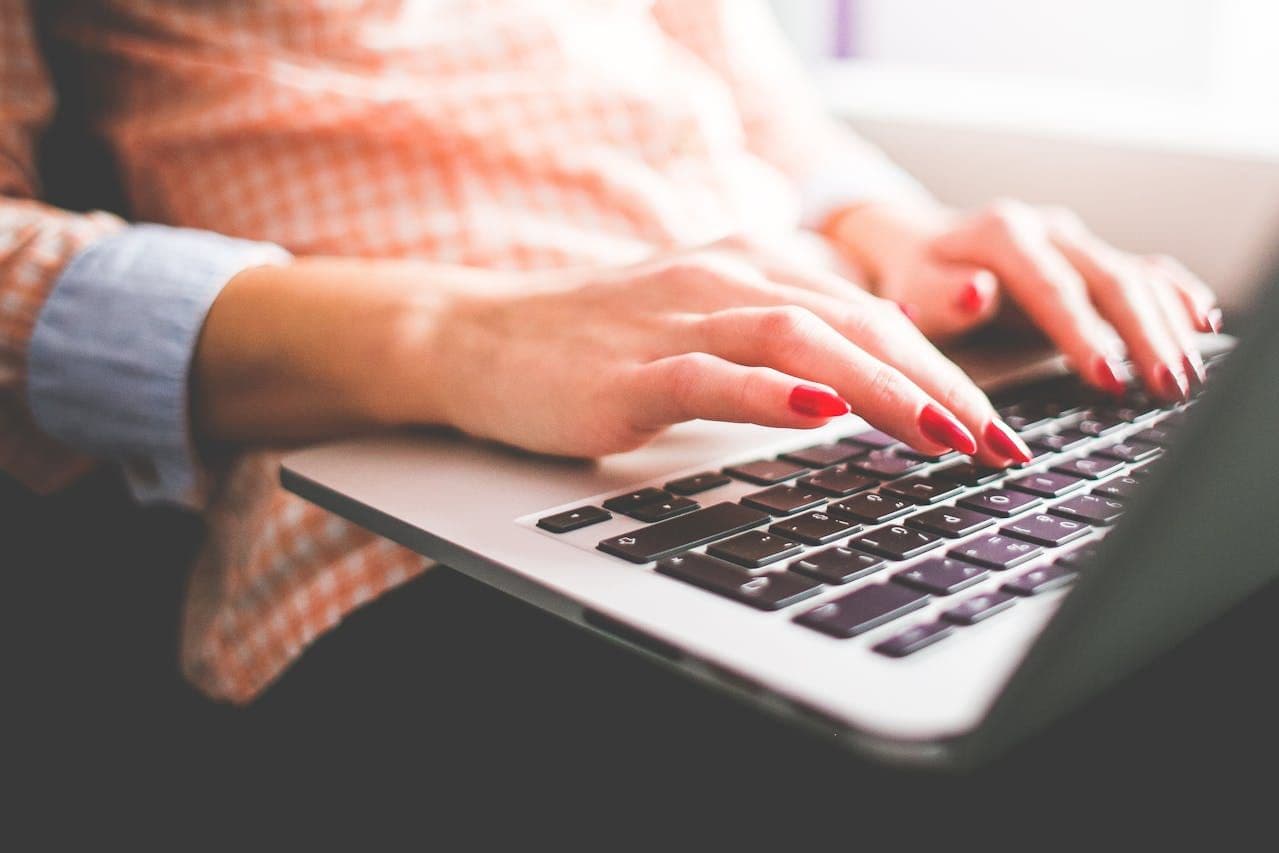 a woman typing on a laptop with red nails