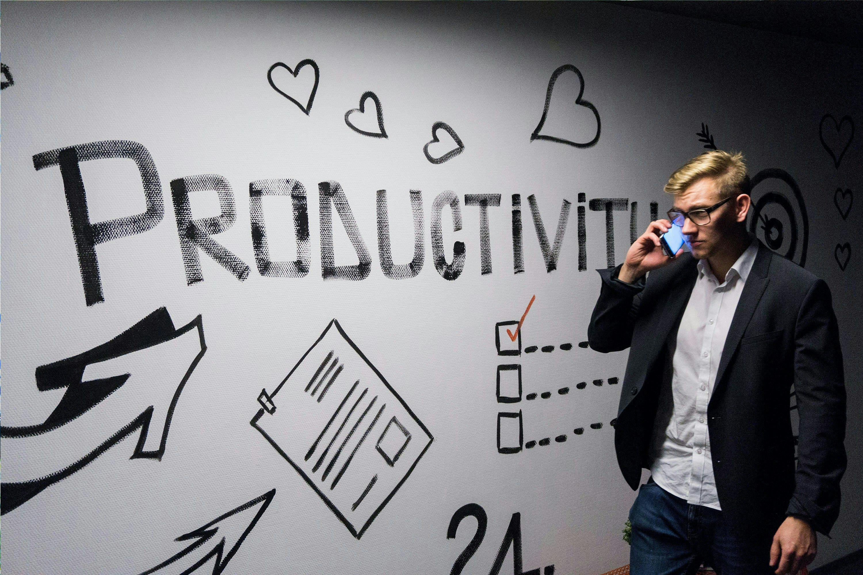 un homme daffaires parlant au téléphone devant un mur avec le mot productivité écrit dessus