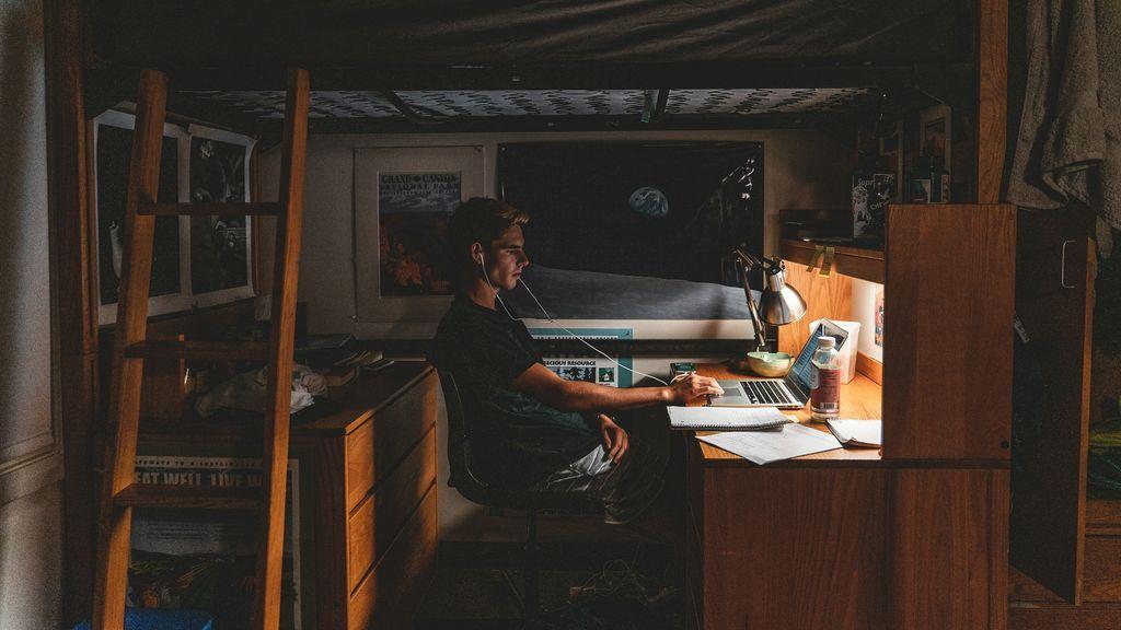 a man working on his laptop in a dorm room