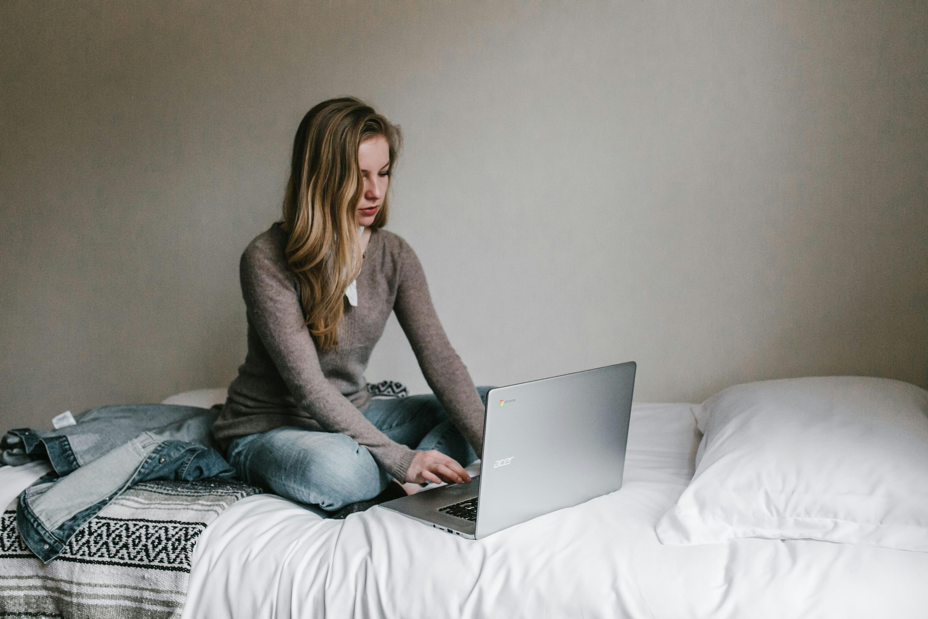 une femme assise sur un lit utilisant un ordinateur portable