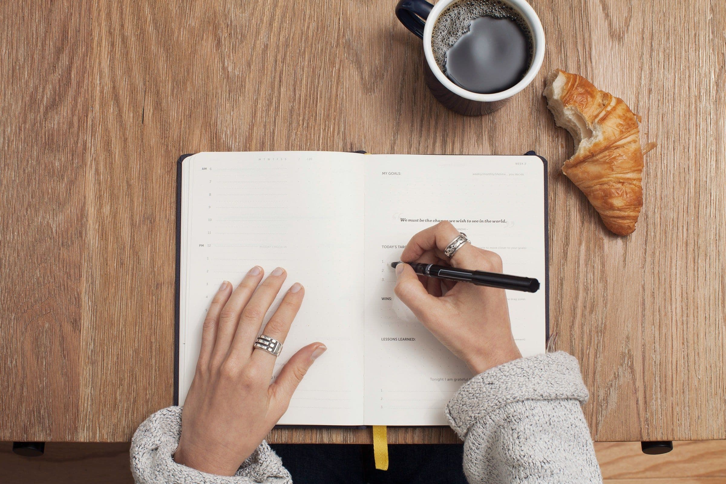 la main dune femme écrivant dans un carnet avec une tasse de café